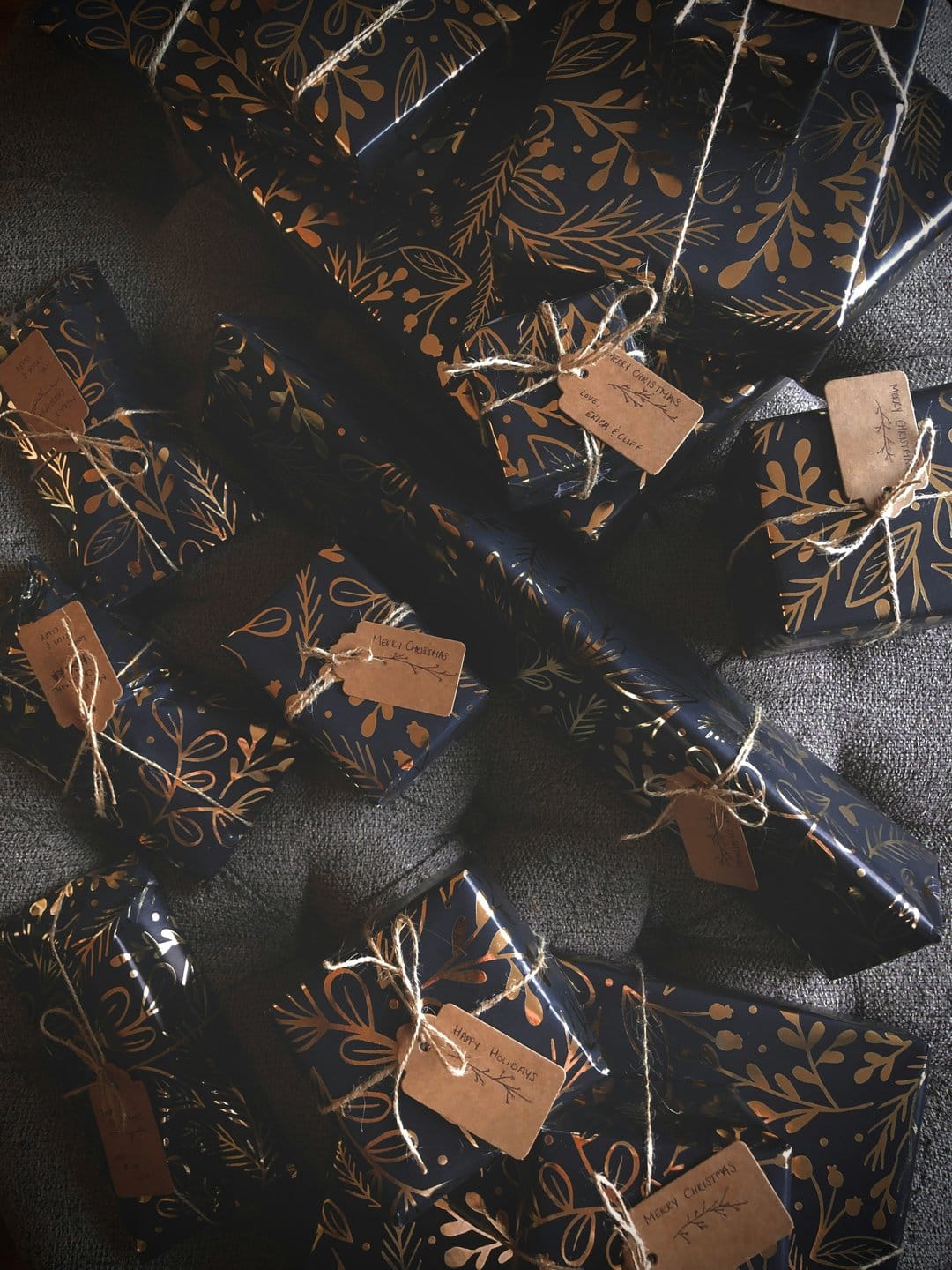 Navy blue gift boxes wrapped in gold foliage patterns feature rustic twine ties and brown paper name tags.