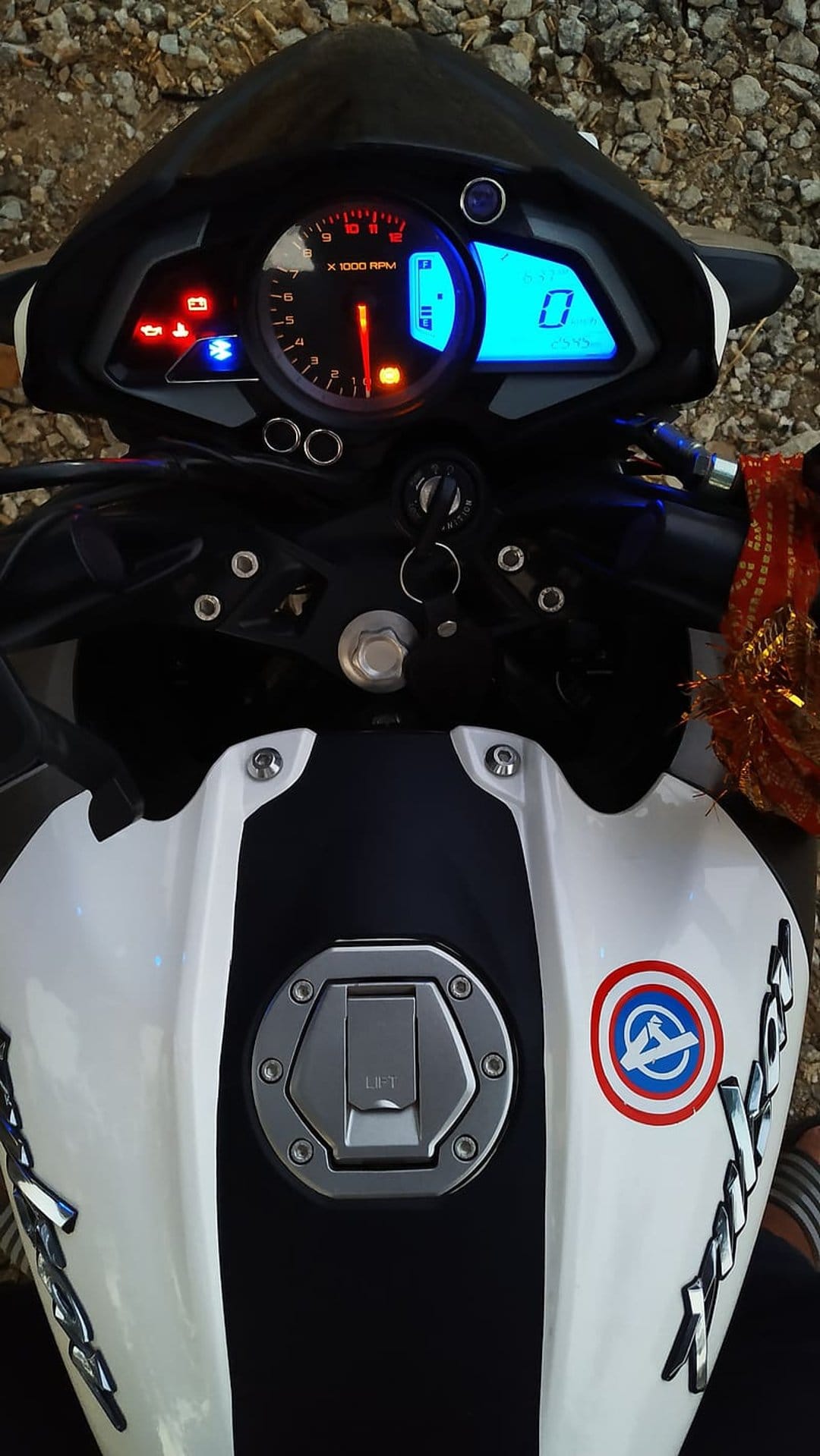 Motorcycle instrument cluster with an analog tachometer and digital display mounted on a white and black fuel tank.