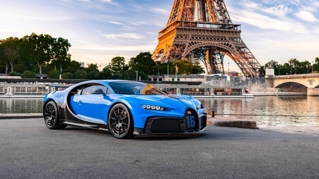 Blue Bugatti Chiron Pur Sport parked by the Seine with the Eiffel Tower at sunset in the background.