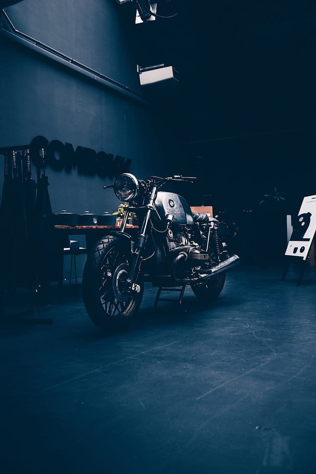 Vintage cafe racer motorcycle with a round headlight parked in a dark industrial studio with soft spot lighting.