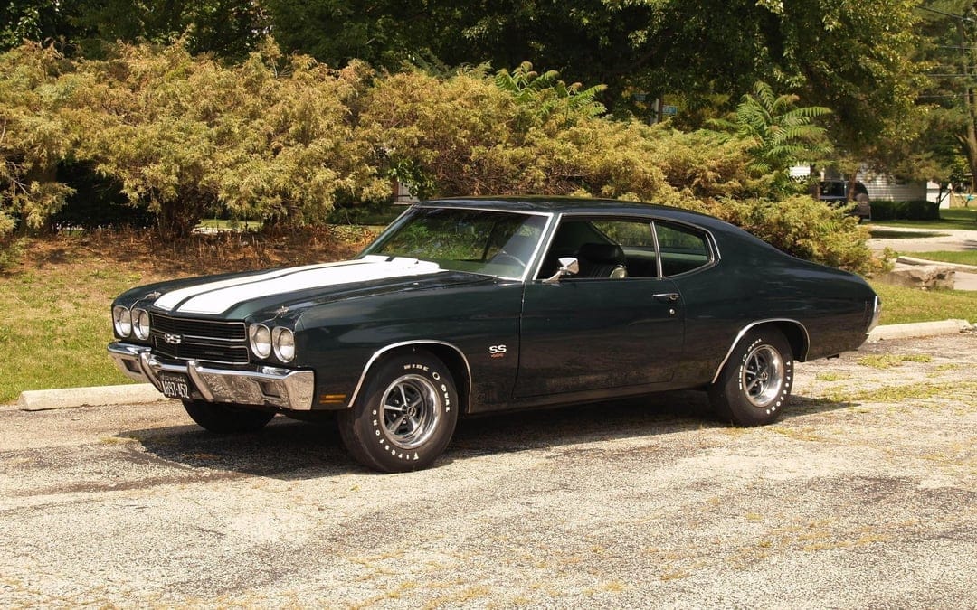 Dark green 1970 Chevrolet Chevelle SS 454 with white racing stripes parked on asphalt under bright daylight.