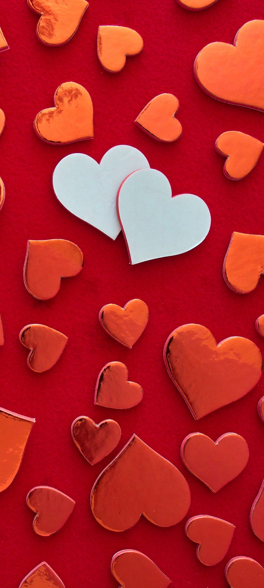 Red and white metallic heart confetti pieces scatter across a textured red background in a flat-lay view.