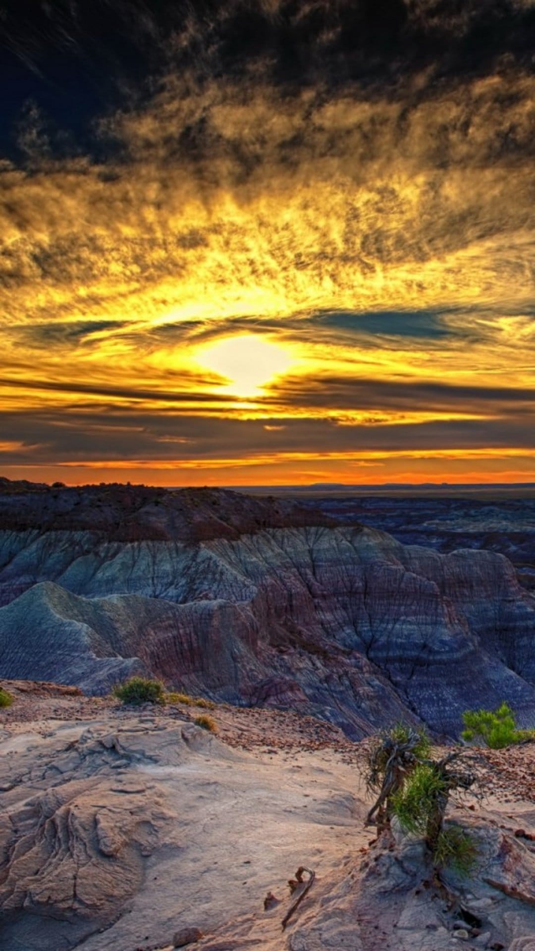 Rugged rock layers and ancient formations glow orange under a dark blue sunset sky in a desert canyon landscape.