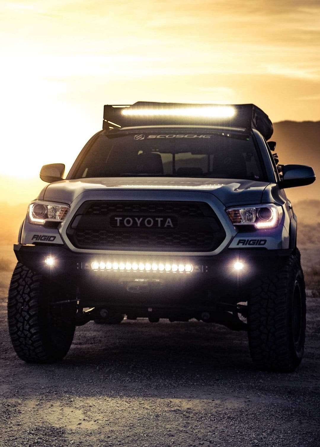 Toyota Tacoma off-road truck with illuminated LED lights in a desert during a golden hour sunset scene.