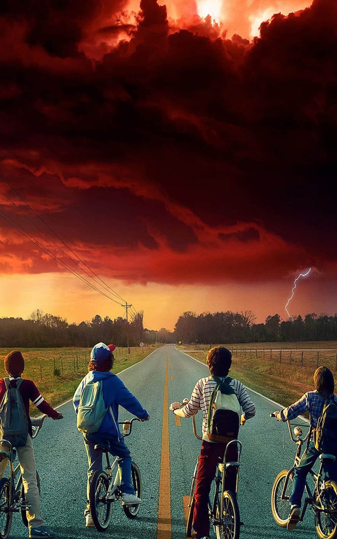 Four children on bicycles stand on a paved road facing a dark red sky with a distant lightning strike.