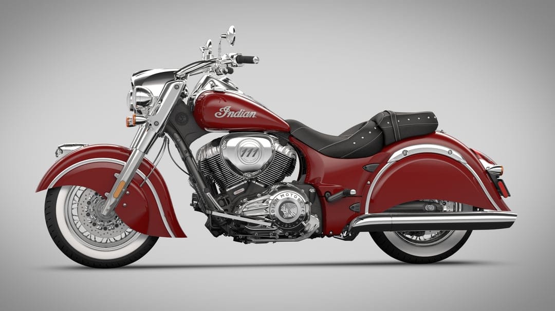 Red Indian cruiser motorcycle with chrome engine and whitewall tires against a soft grey studio background.