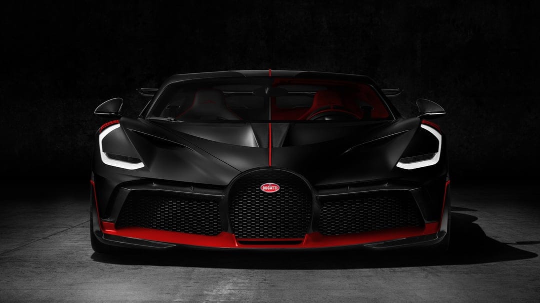 Matte black Bugatti Divo hypercar front view with red accents and glowing white LED headlights in a dark studio.