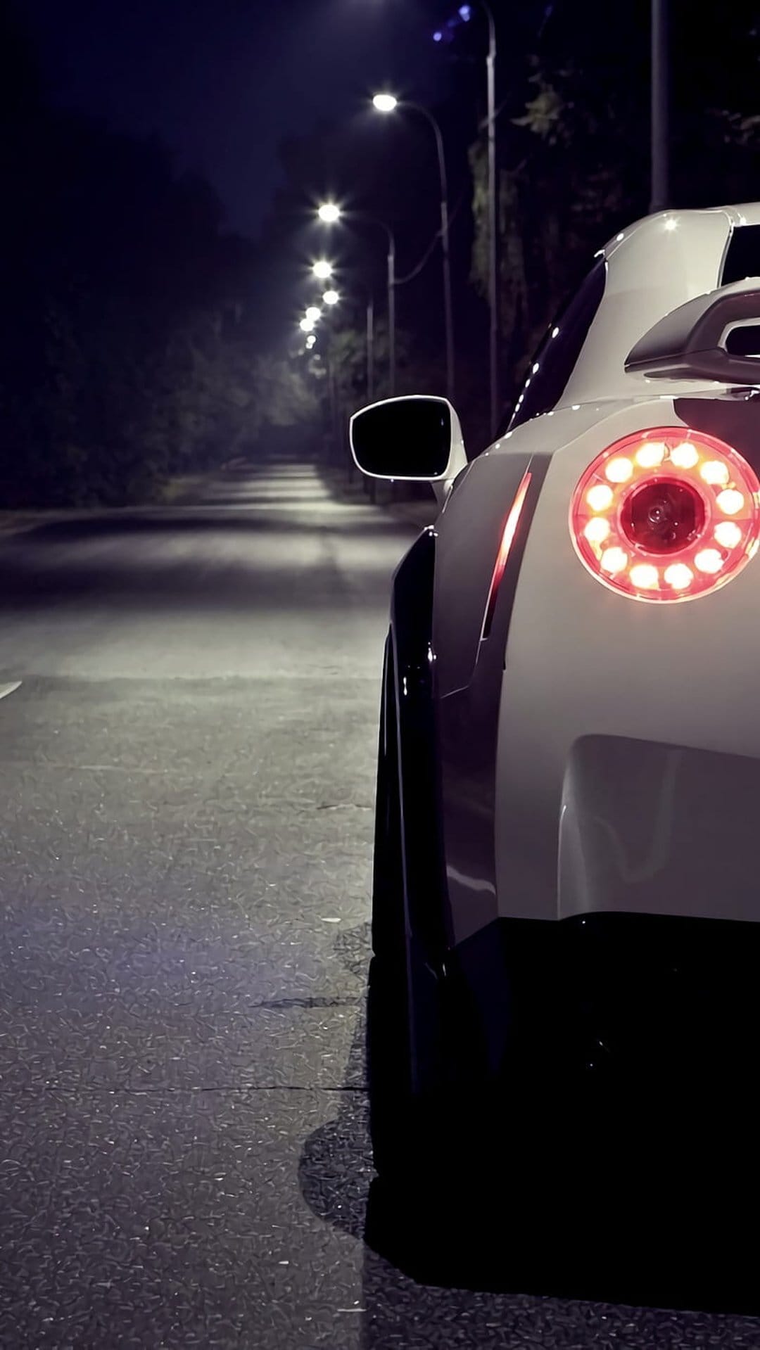 White sports car taillights glowing red on a wet asphalt road at night with distant streetlights and reflections.