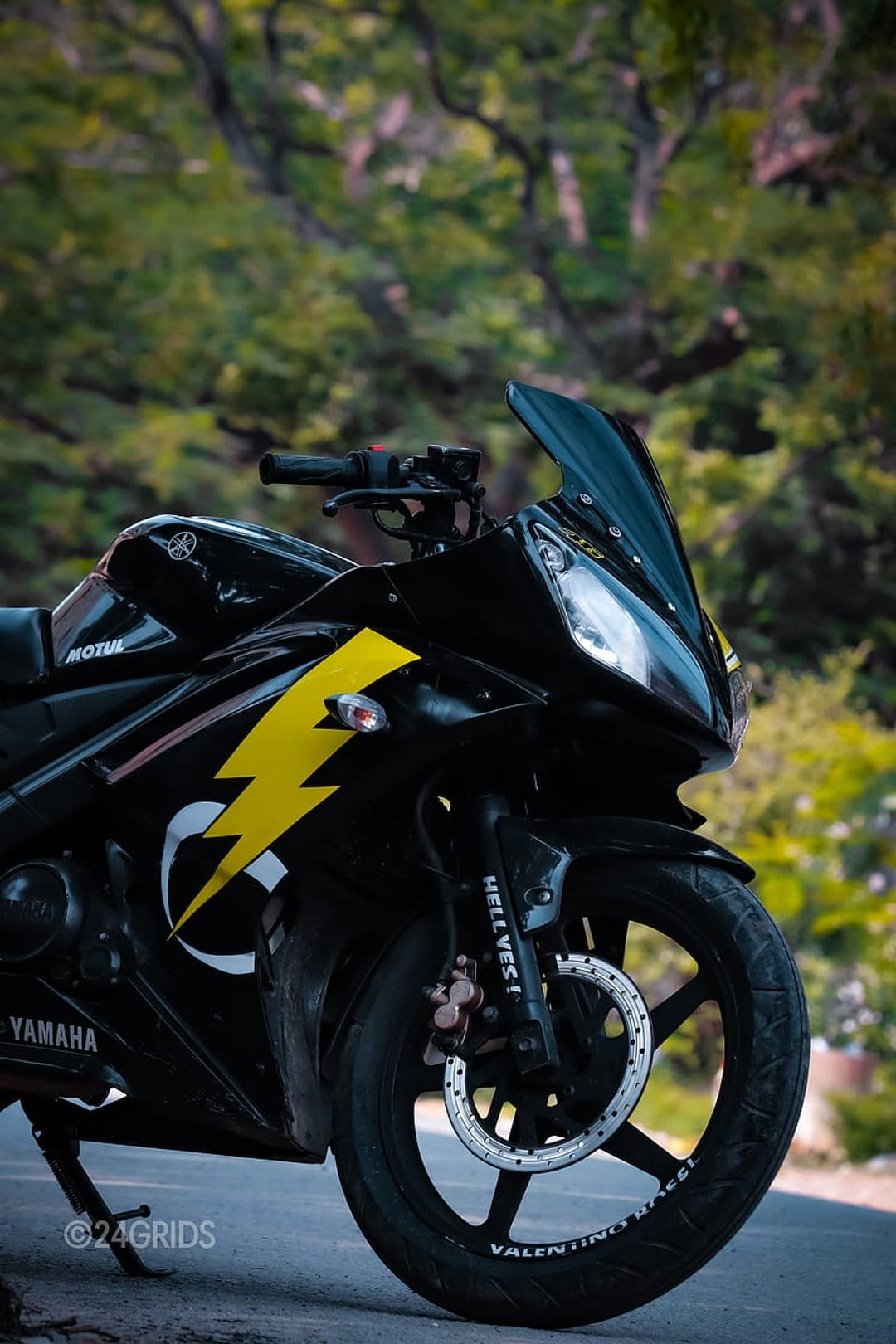 Black Yamaha R15 motorcycle with a yellow lightning bolt graphic and disc brake against a blurred green background.