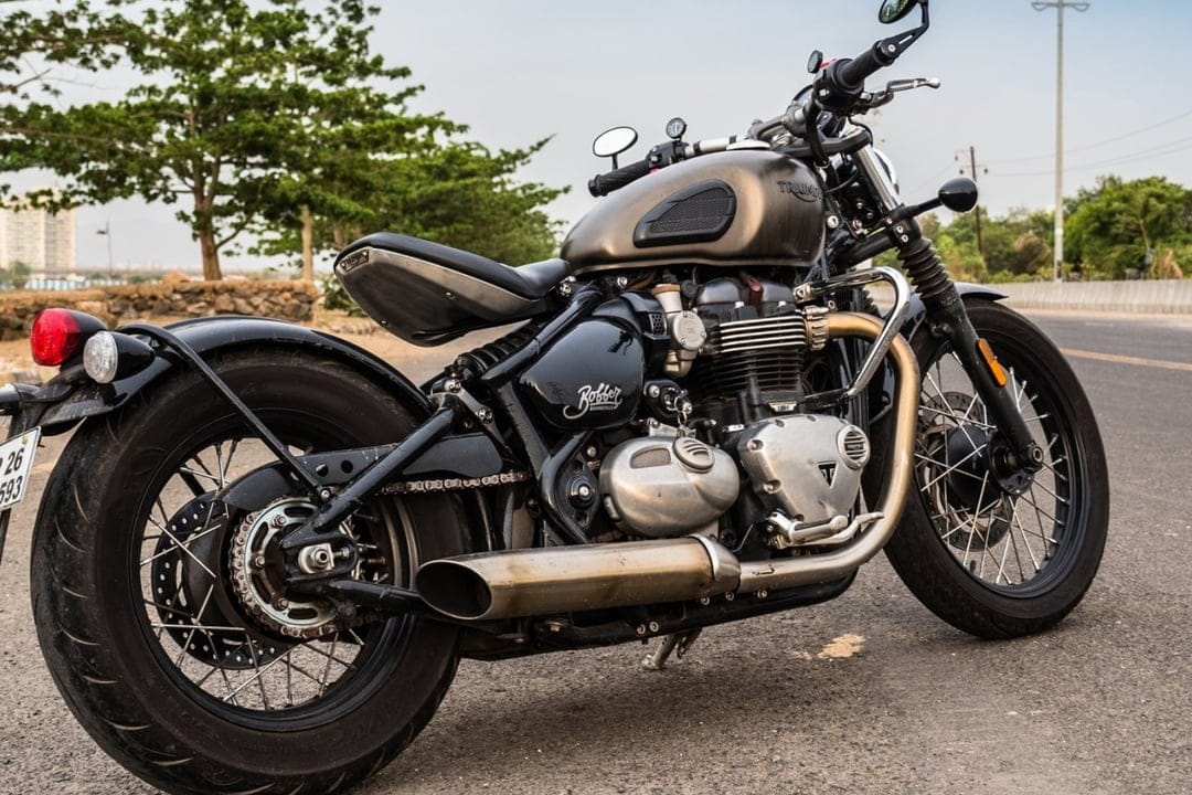 Custom Triumph Bonneville Bobber with a metallic tank and floating seat parked on a roadside in daylight.