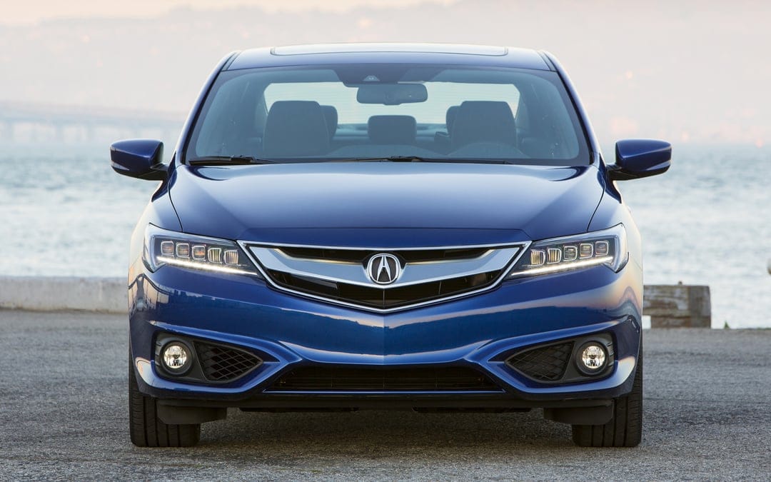 Front view of a blue Acura ILX with LED headlights on a pier with water and a distant bridge in the background.