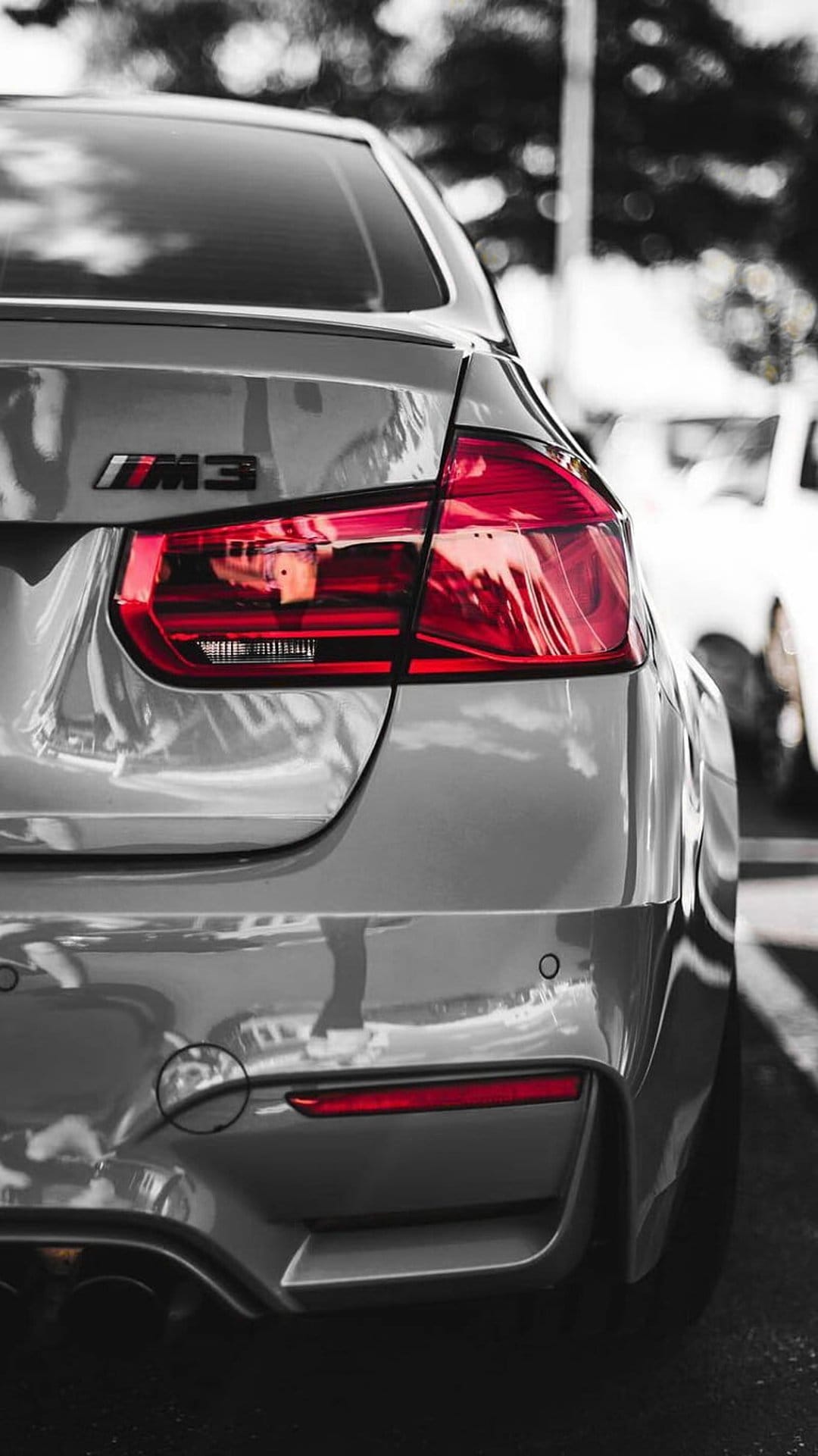 BMW M3 silver rear tail light and metallic emblem displaying intricate LED textures and soft reflections.