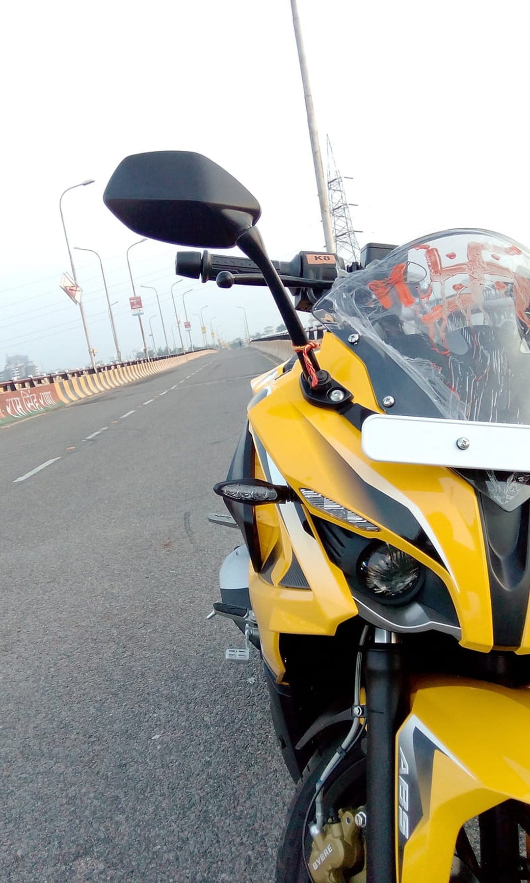 Yellow sportbike parked on a bridge roadway under an overcast sky with handlebars and mirrors in focus.