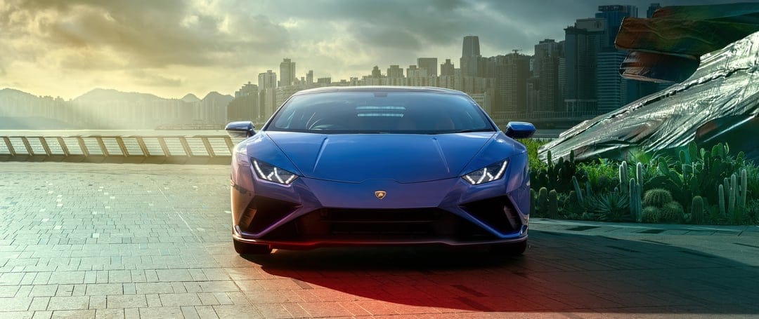 Blue Lamborghini Huracan Evo parked on a city waterfront during a golden hour sunset with red underglow.