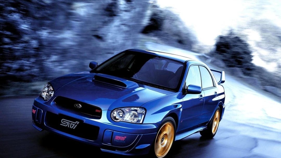 Blue Subaru WRX STI with gold wheels driving fast on a road with heavy motion blur in the background.
