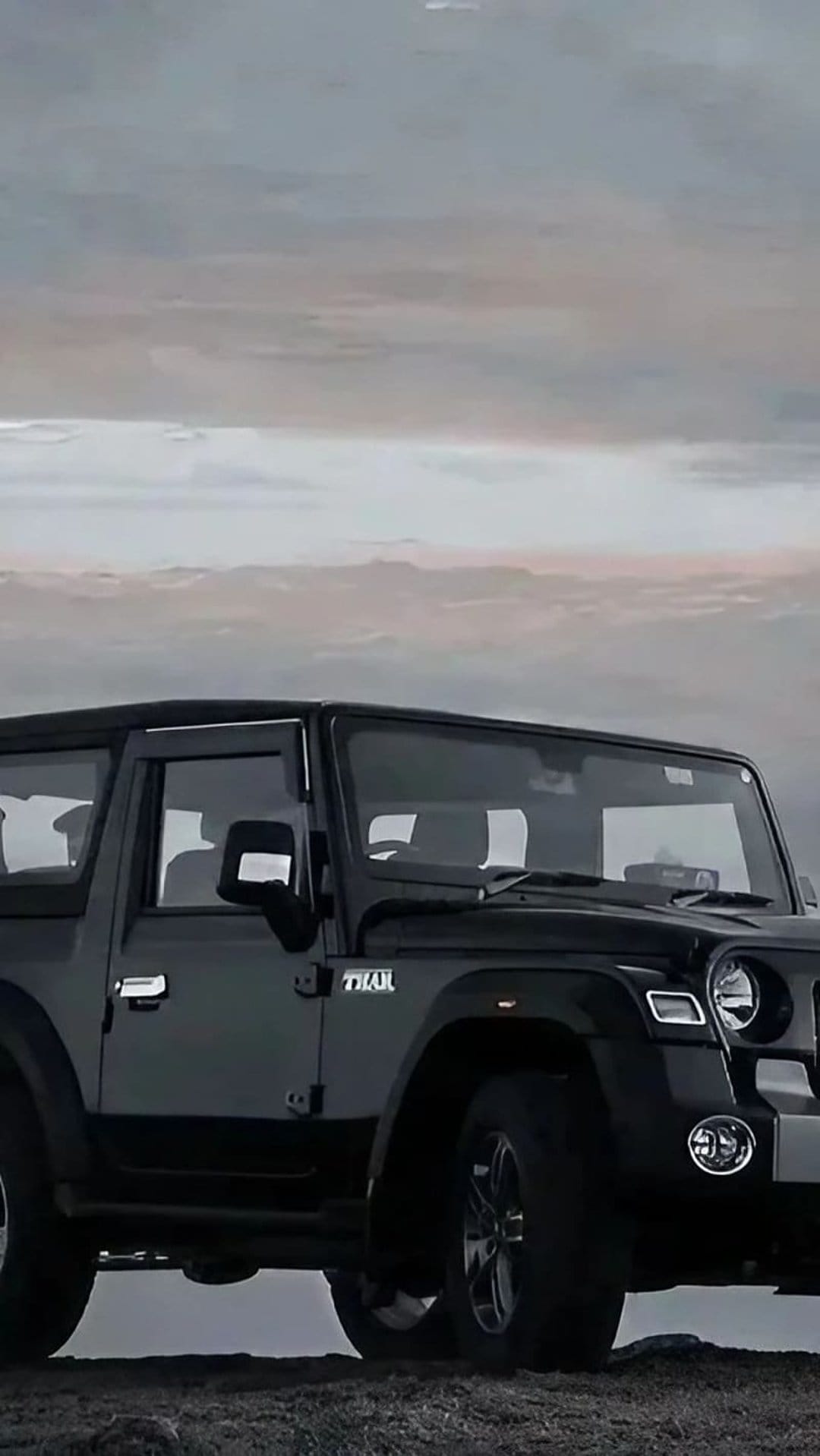 Black Mahindra Thar SUV parked under a heavy, dramatic sky with soft light reflecting off its dark metallic body.