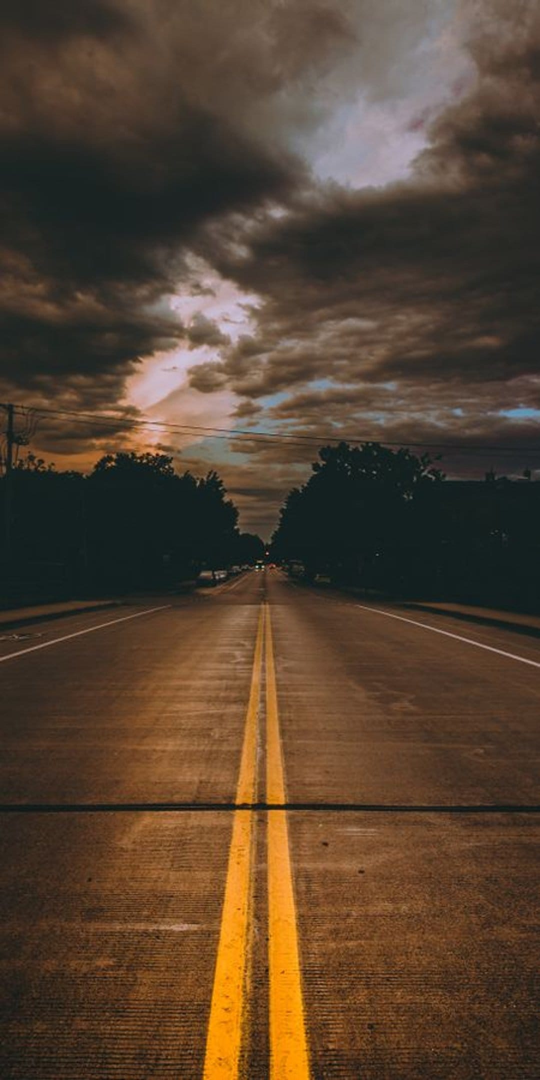 Straight asphalt road with double yellow lines vanishing into a vibrant orange and purple sunset horizon.