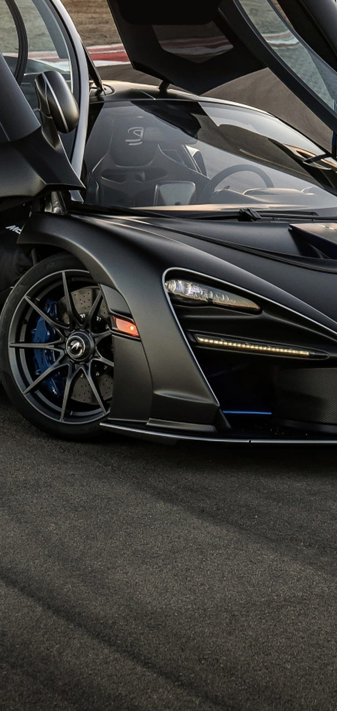 McLaren Senna sports matte black paint, open butterfly doors, carbon wheels, and bright blue brake calipers.