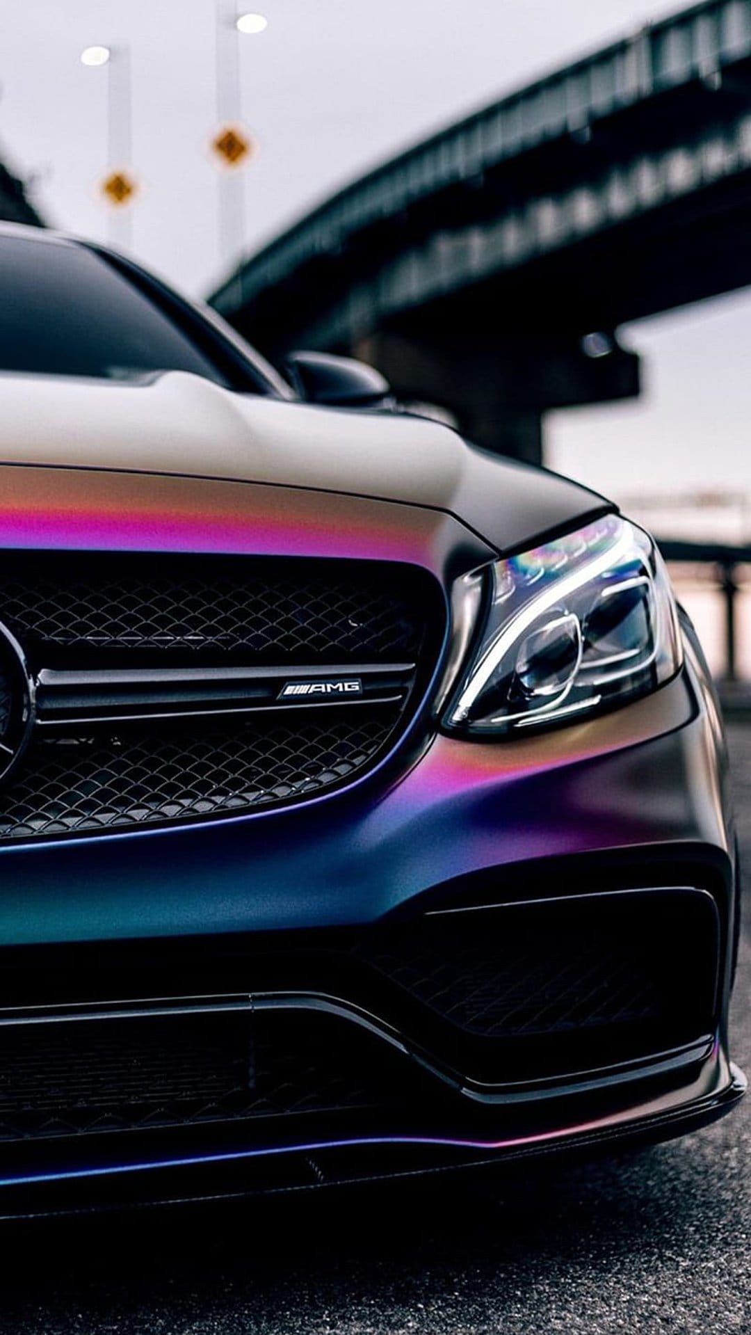Mercedes-AMG C 63 S Coupe with iridescent purple paint and glowing LED headlights on an asphalt street.