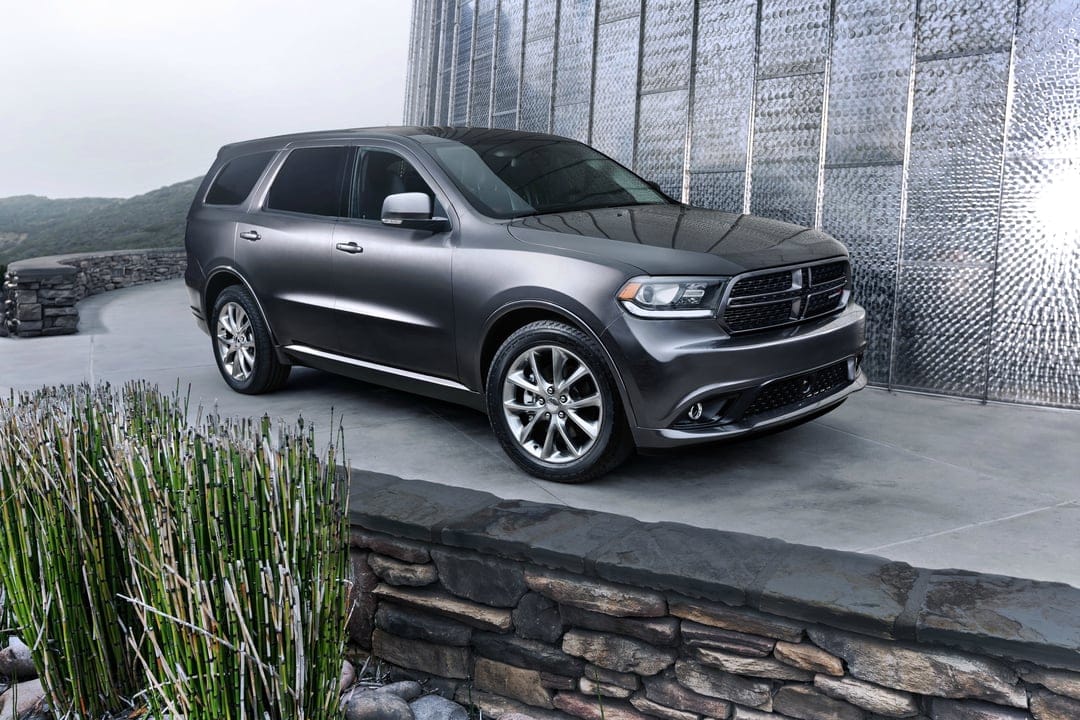 Dark gray Dodge Durango SUV parked on a stone path beside a textured silver wall and green horsetail plants.