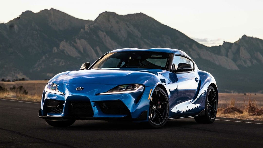 Blue Toyota Supra parked on a road with craggy mountains in the background during golden hour.