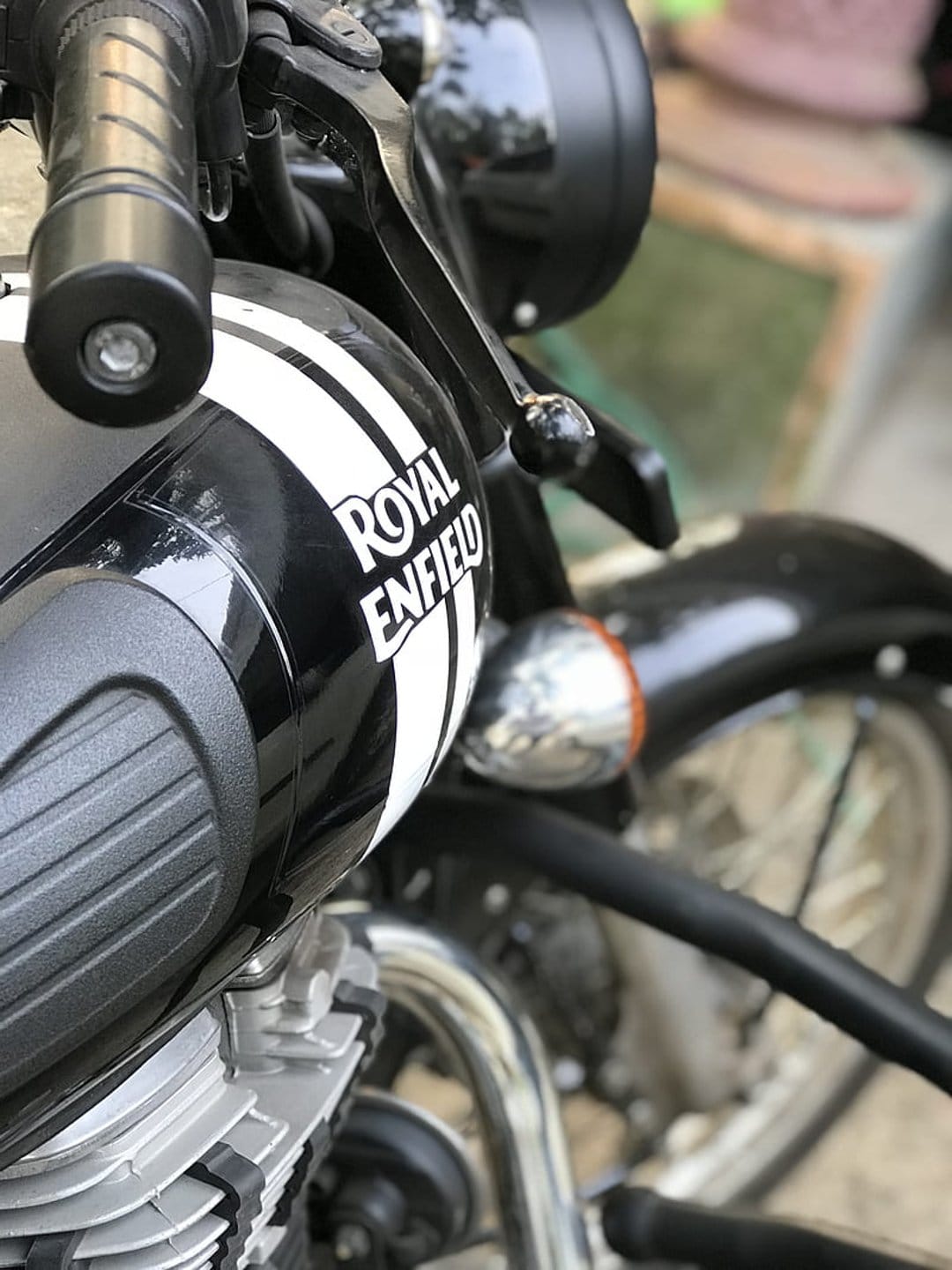 Royal Enfield motorcycle fuel tank with white stripes, chrome handlebars, and leather brake lever in close-up.