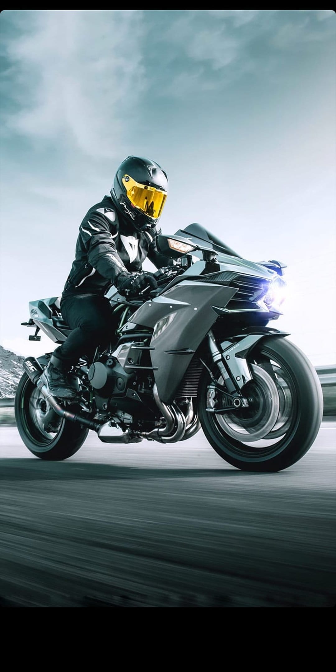 Kawasaki Ninja H2R rider in a black racing suit leaning on a high-speed motorcycle on a mountain road.