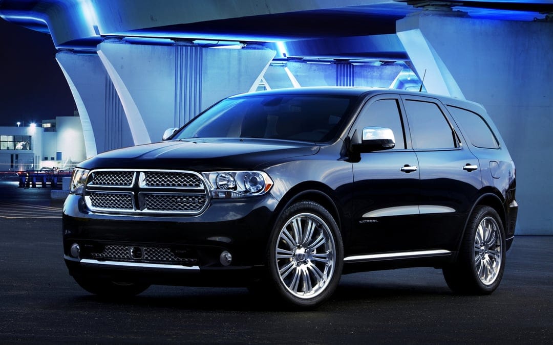 Black Dodge Durango SUV with chrome wheels parked under a bridge illuminated by bright blue neon lights at night.