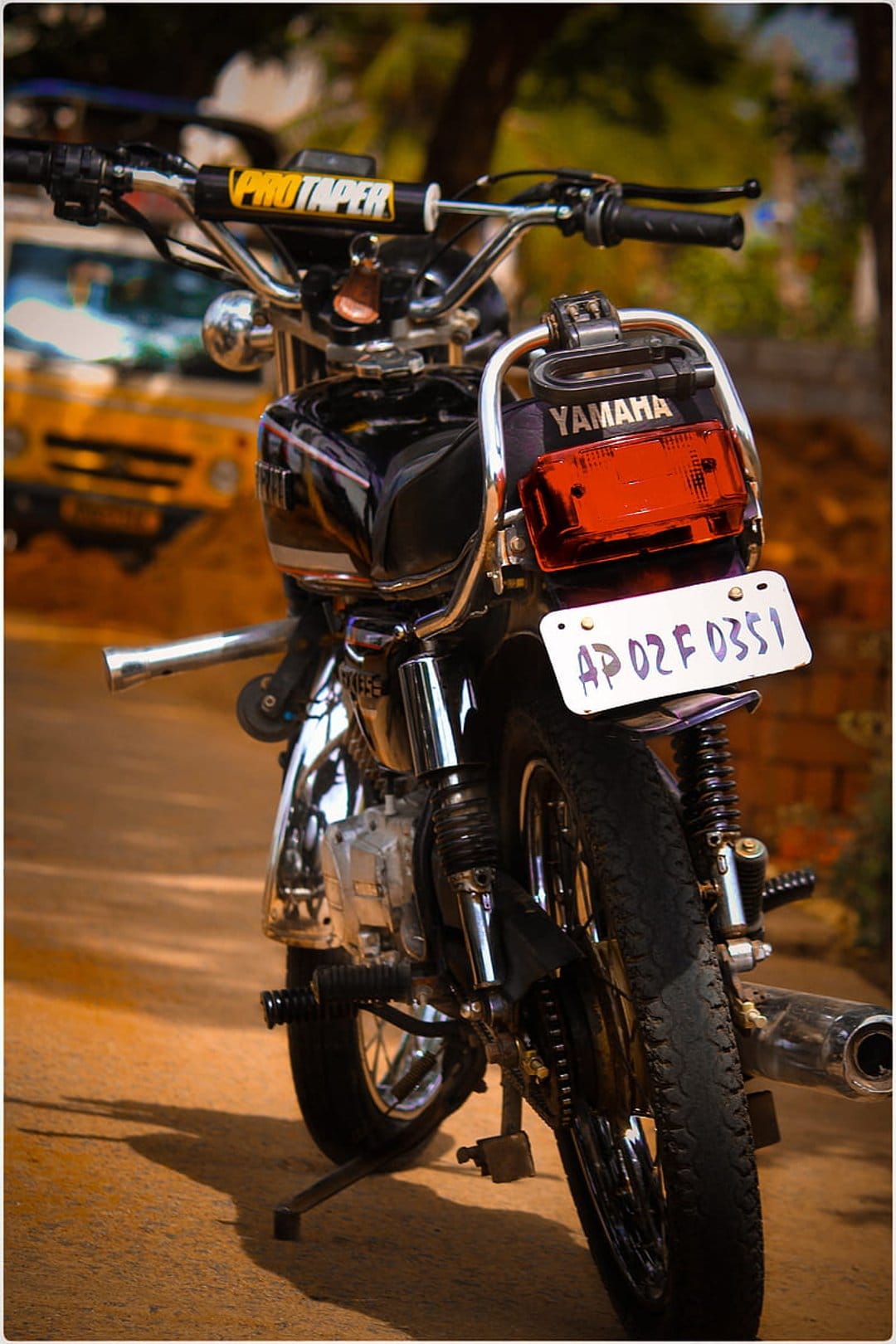 Yamaha motorcycle rear view with ProTaper handlebars, chrome grab rail, and red tail light in sunlight.
