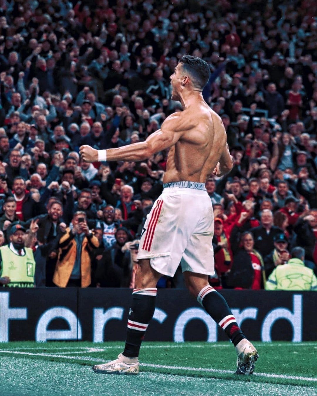Cristiano Ronaldo shirtless from behind, showing muscular back and white shorts in a crowded stadium celebration.