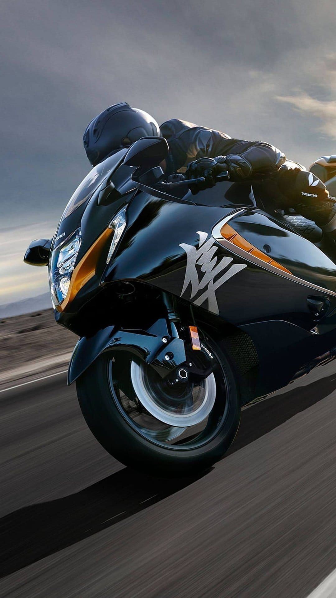 Suzuki Hayabusa sportbike leans into a high-speed run on an open road beneath a moody and overcast sky.