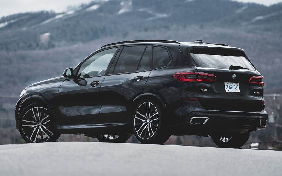 Black BMW X5 SUV parked on an asphalt road against a backdrop of misty mountains in soft daylight.