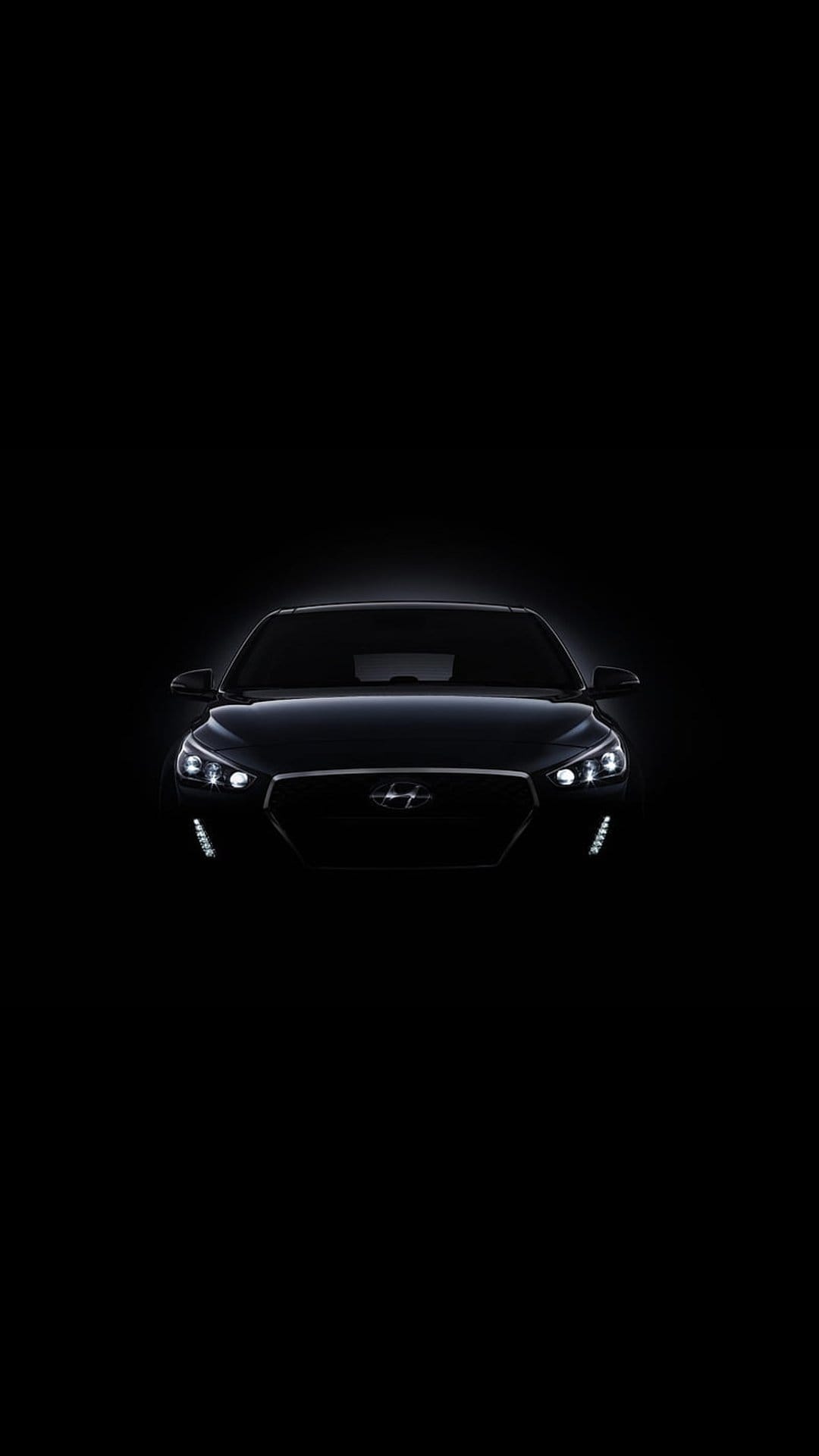 Hyundai i30 front view with glowing LED headlights and a mesh grille visible against a pitch black background.