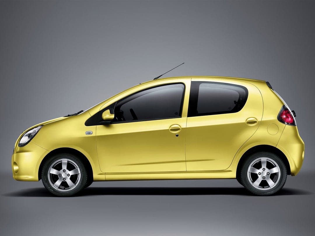 Side view of a bright yellow compact hatchback with silver wheels against a solid gray studio background.