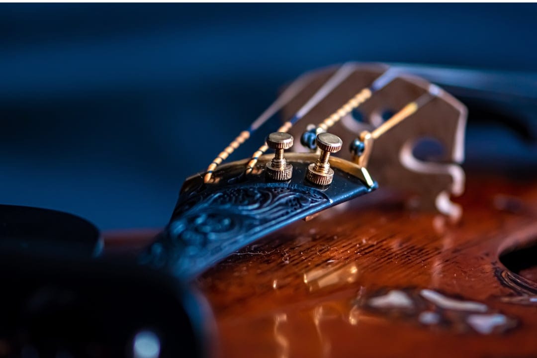 Hand-carved ebony violin scroll featuring gold-plated tuning pegs against a deep blue atmospheric background.