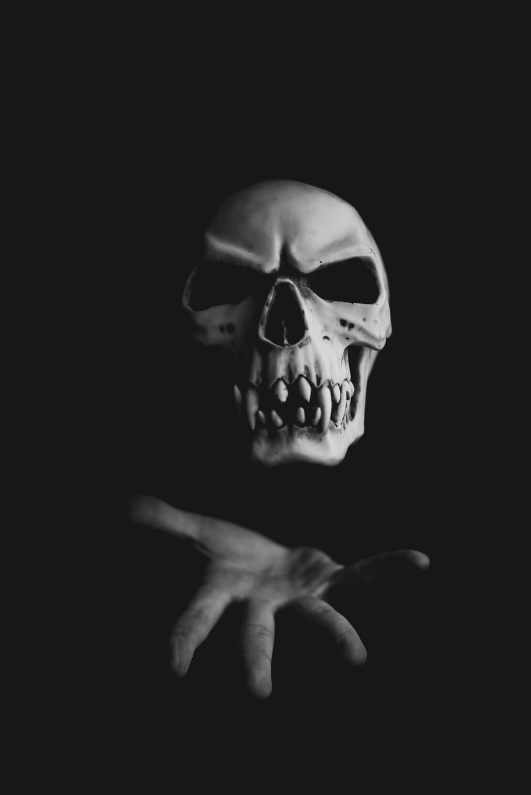 Human skull floats above an outstretched hand in high-contrast black and white against a dark background.