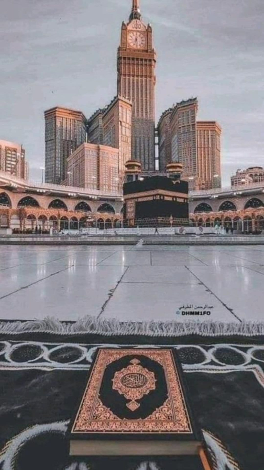 Quran on a prayer mat overlooks the Kaaba and the massive Makkah Clock Tower under a clear sky.
