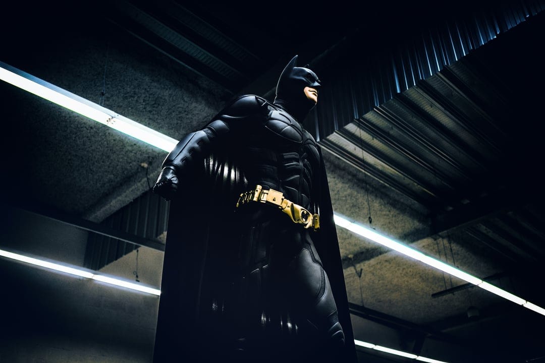 Batman statue in black and gold armor stands under fluorescent ceiling lights with deep industrial shadows.