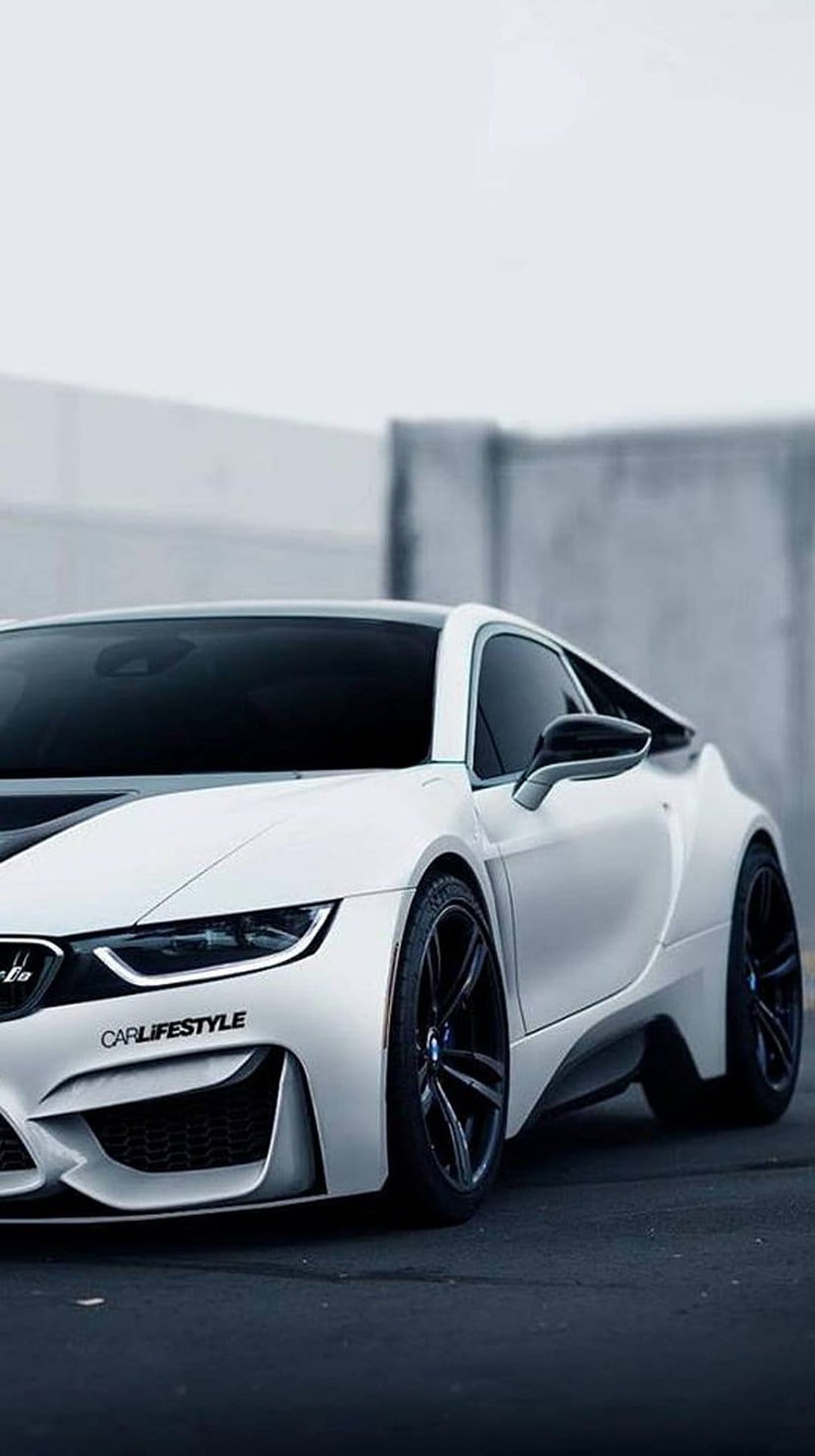 White BMW i8 sports car parked against a concrete wall, showcasing its aerodynamic curves and tinted windows.