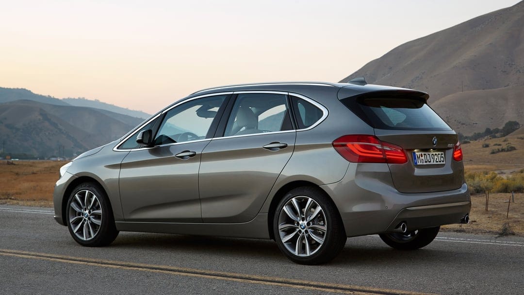 Rear view of a metallic BMW 2 Series on a roadside with soft mountain peaks and a pale sunset sky in the distance.