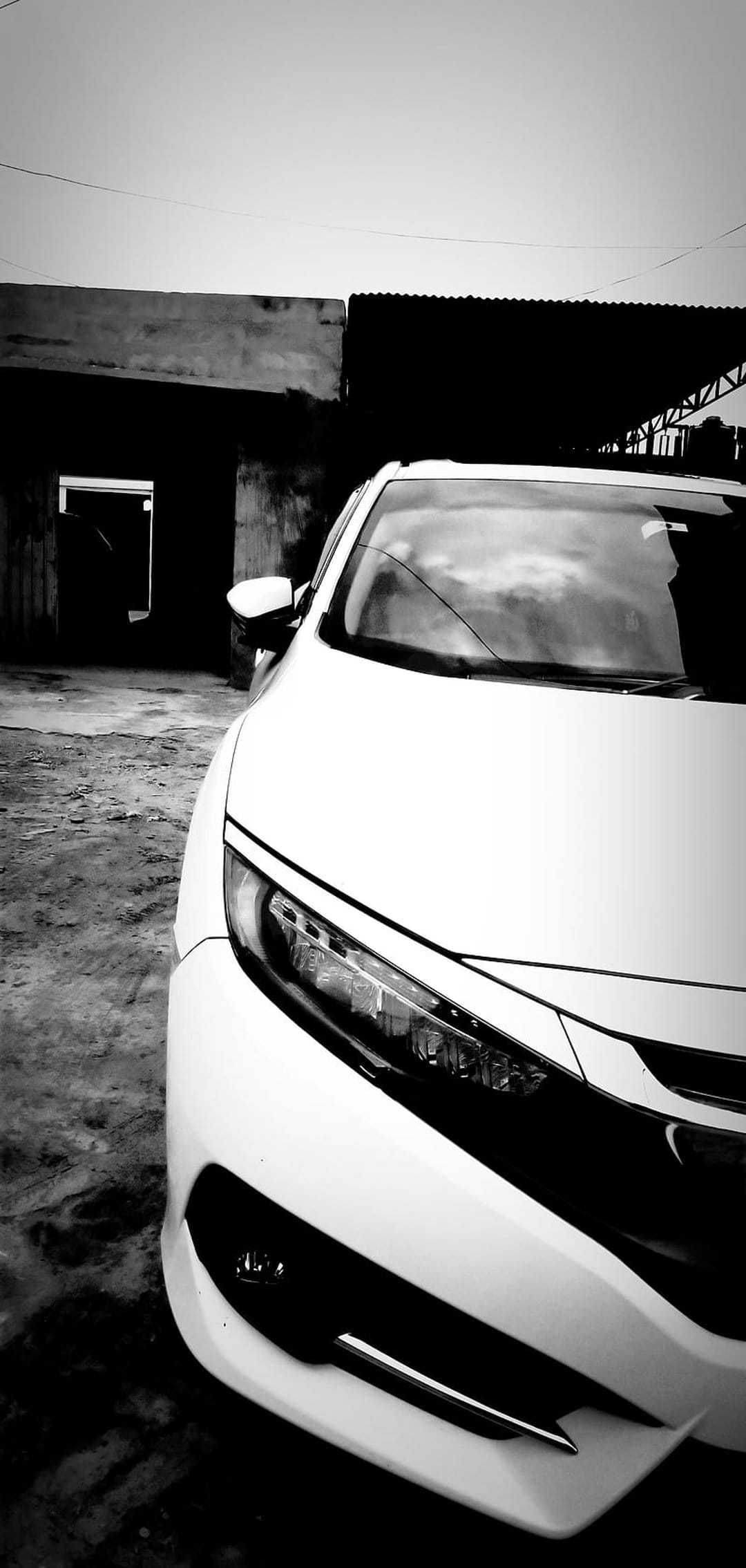White car front view with illuminated headlights and sleek body lines in a high-contrast monochrome urban setting.
