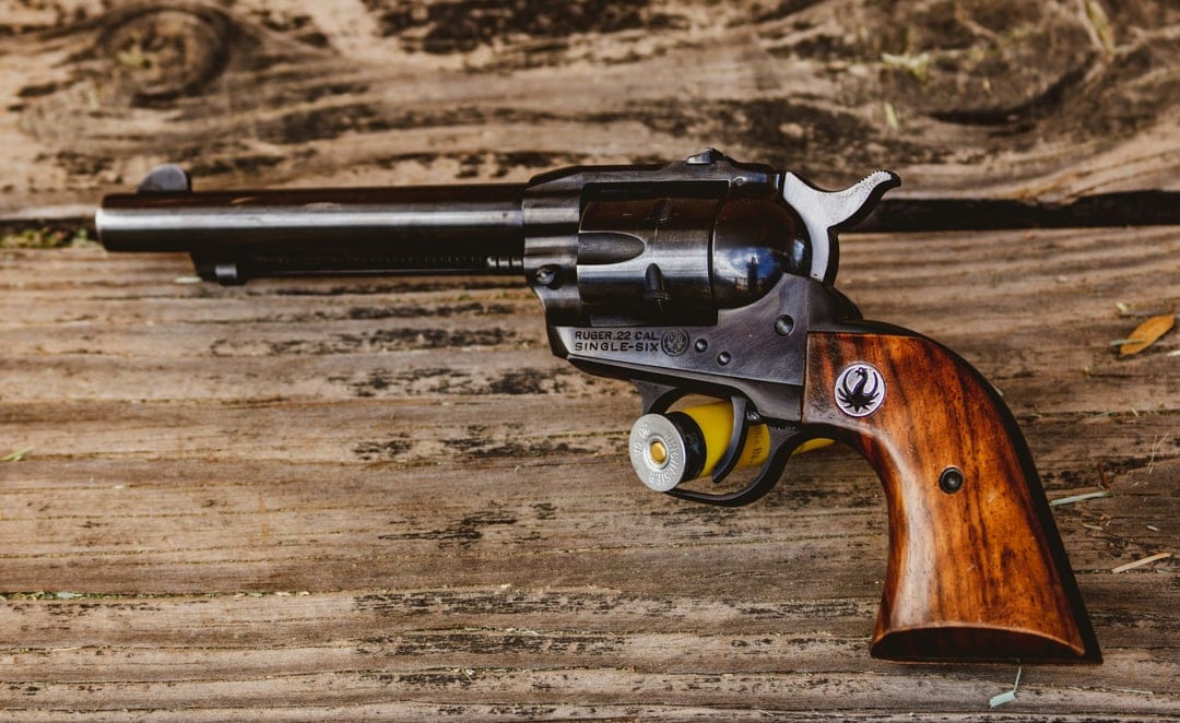 Antique single-action revolver with dark blued steel and wooden grips lying on a rustic timber surface.