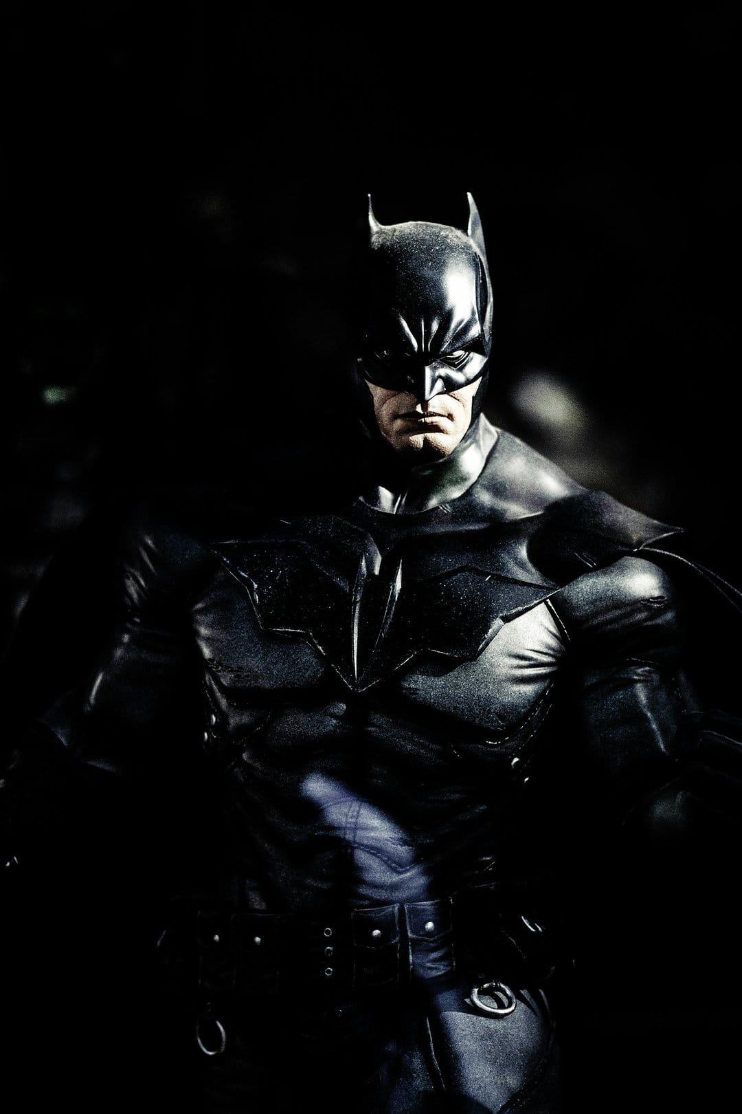 Batman armored chest plate featuring a matte black bat symbol, illuminated by sharp side lighting and deep shadows.