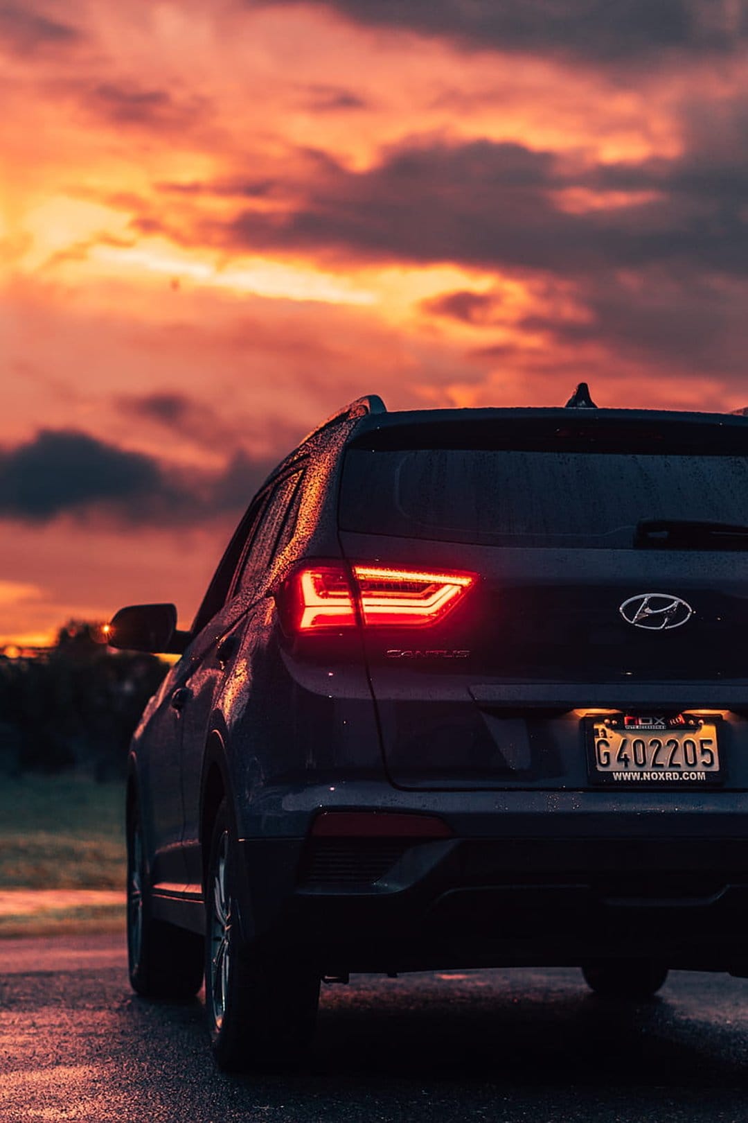 Hyundai Elantra sedan on wet asphalt reflecting a dramatic orange sunset sky with glowing red taillights.