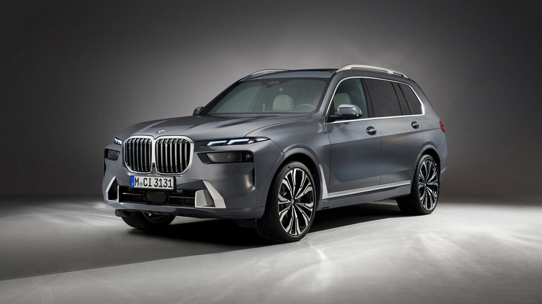 Gray BMW X7 luxury SUV in a studio with bright headlights, chrome grille, and large multi-spoke wheels.