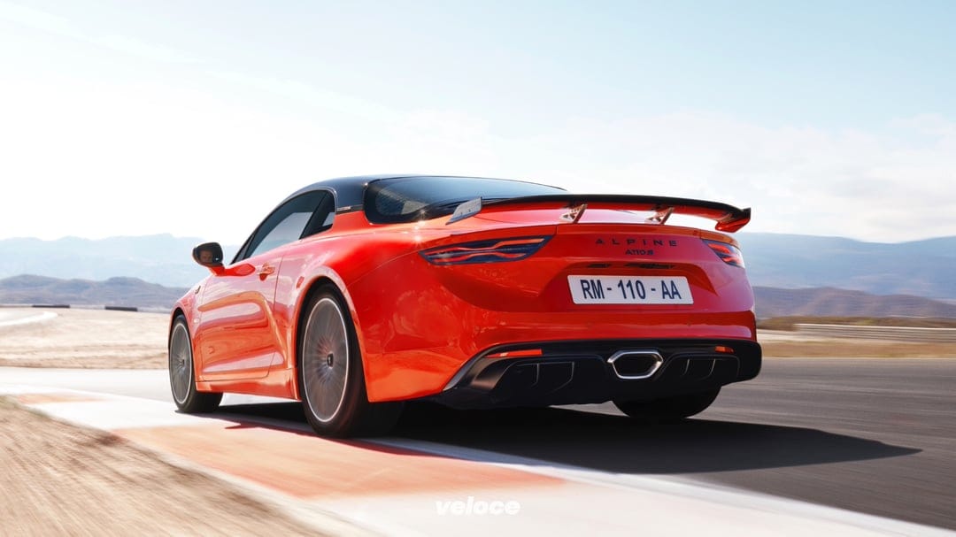 Orange Alpine A110S sports car racing on a track with mountain background and clear sky during daylight.