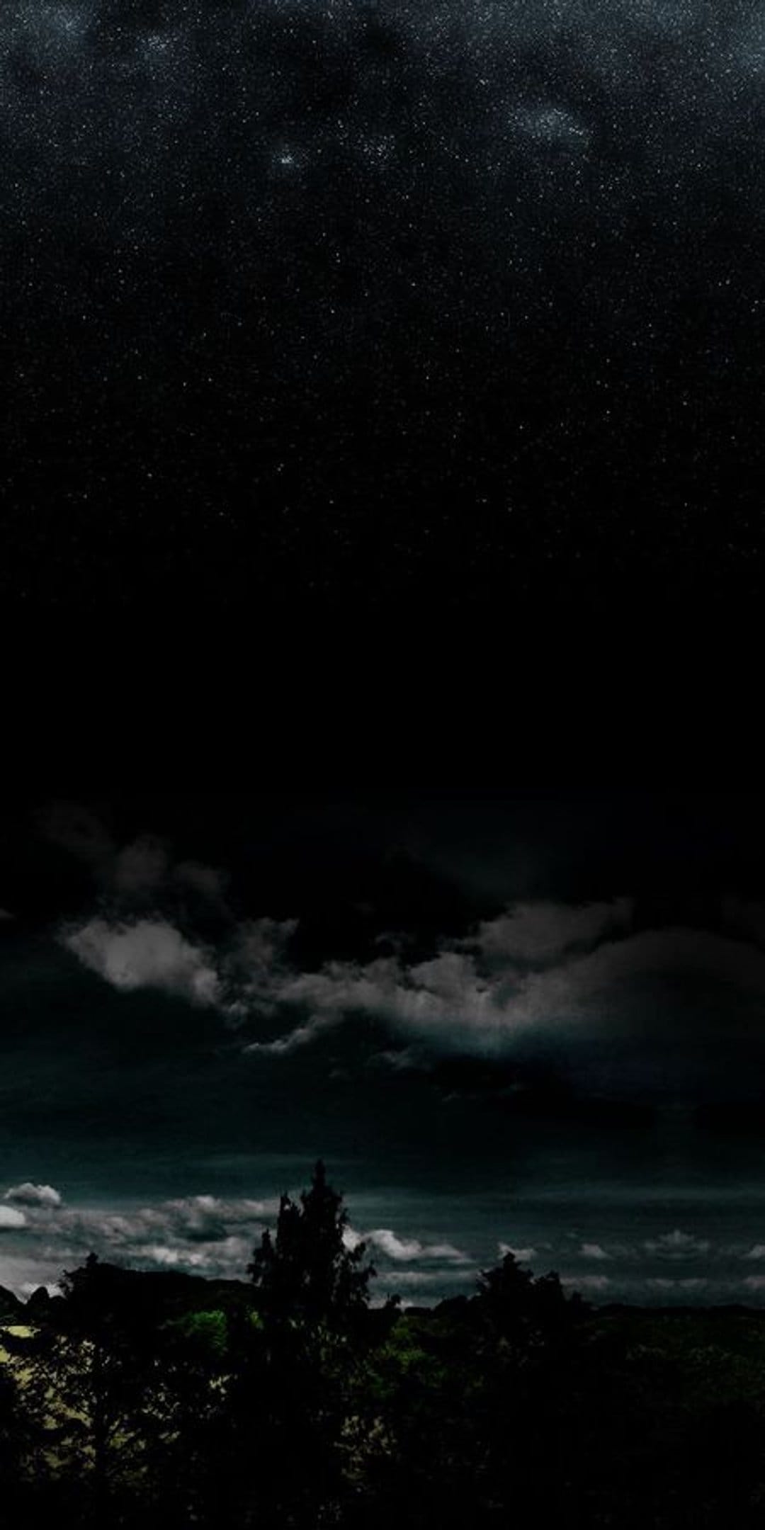 Millions of stars illuminate the dark sky over heavy clouds and a silhouetted forest landscape at night.