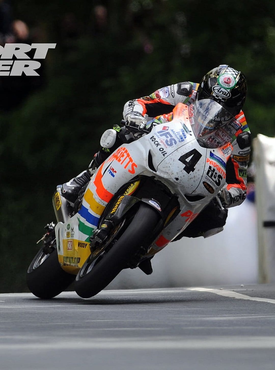 Motorcycle racer in orange leathers leans into a track turn with white smoke trailing from the rear wheel.