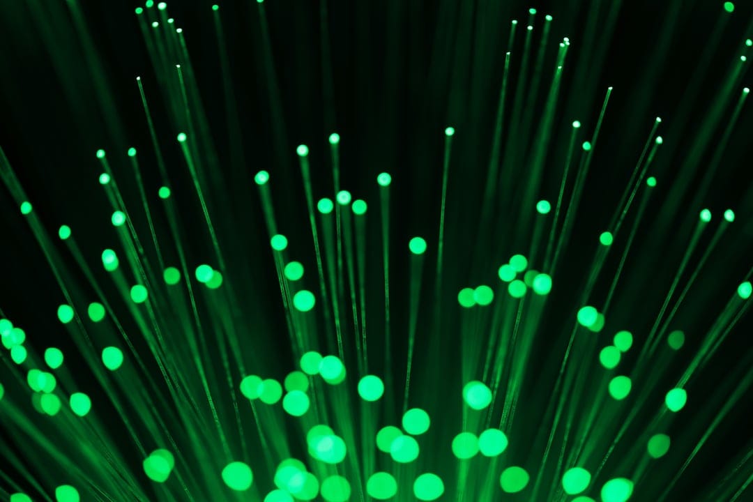 Glowing green fiber optic strands with luminous tips and soft bokeh circles against a dark background.