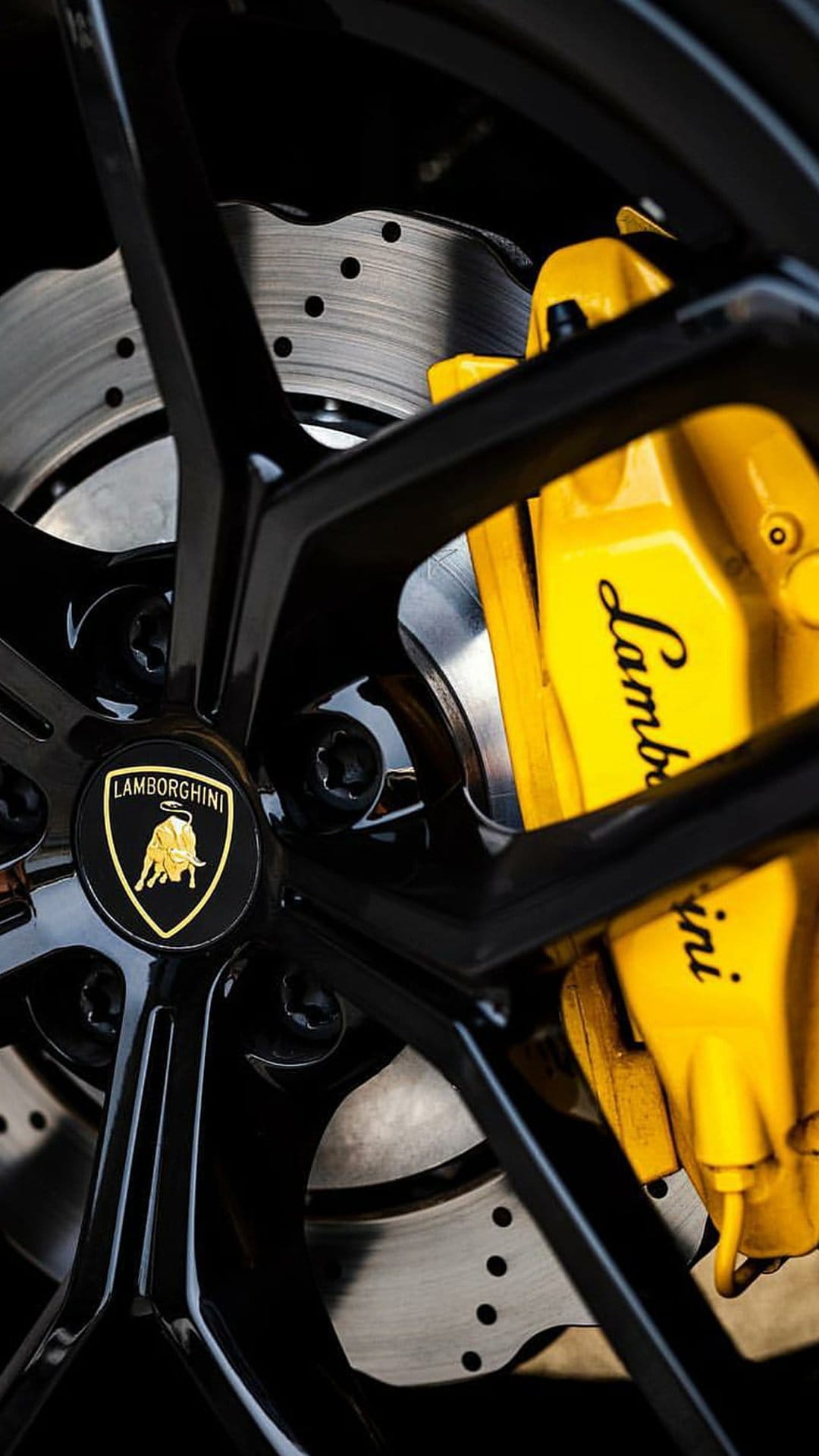 Black multi-spoke wheel with a yellow brake caliper and perforated ceramic disc on a high-performance supercar.